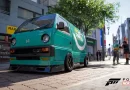 Furgoneta compacta estilo Kei car (Honda Acty) de color verde turquesa, rebajada de suspensión y con llantas deportivas, aparcada en una calle adoquinada junto a edificios y vegetación. Forza horizon 6