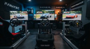 Estudio de simracing profesional con tres cockpits alineados. De izquierda a derecha: un cockpit Fanatec, uno Moza Racing con asiento Trak Racer, y uno Thrustmaster. Cada uno tiene volantes de la marca y pantallas corriendo Assetto Corsa Competizione, con los logotipos de FANATEC, MOZA y THRUSTMASTER visibles en la pared.